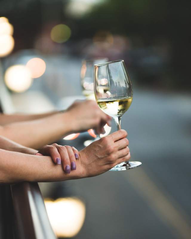 Two glasses of white wine are held out over Jianna's patio with a blurred view of downtown at dusk.