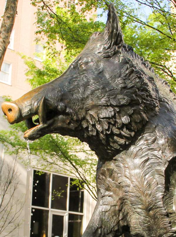 Statue of a boar in front of buildings and trees.