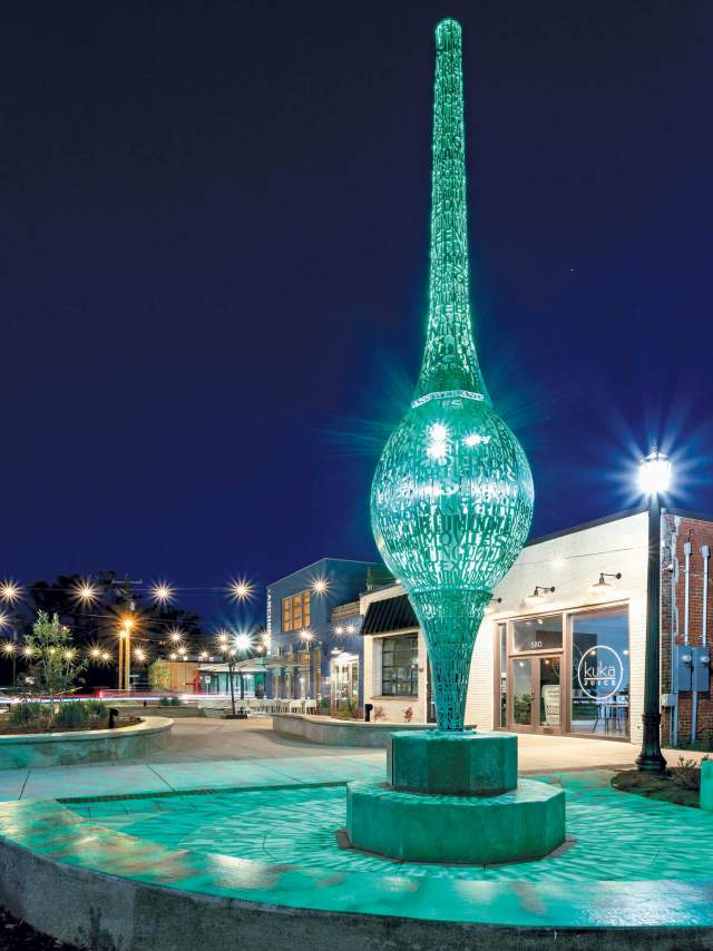 The Spindle sculpture lit up in a greenish aqua hue at night in The Village, a western area of Greenville, SC.