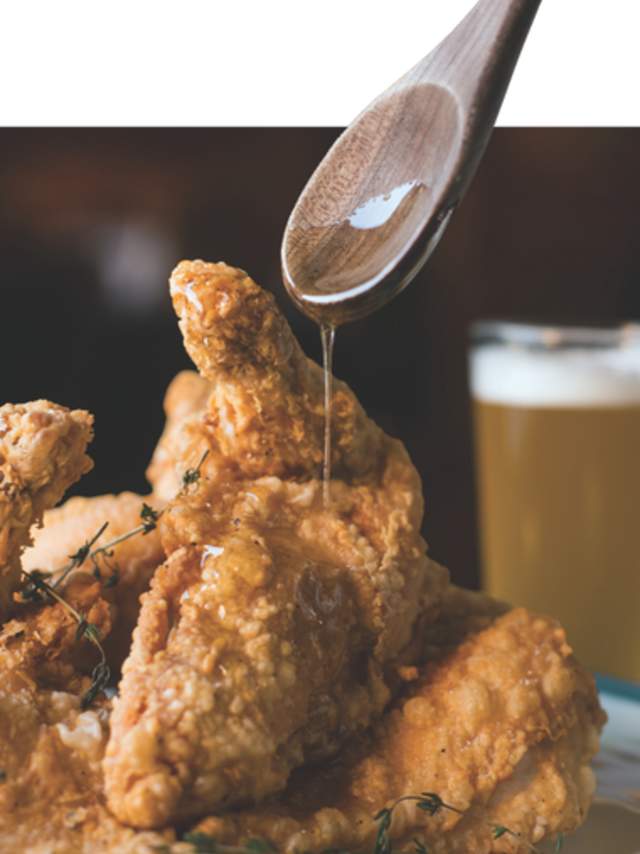 Clipped image of honey being drizzled on fried chicken with a beer in the background at Soby's New South Cuisine.