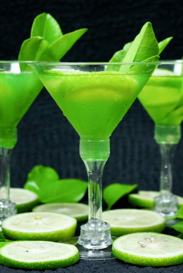 Three martinis with lime sit atop a black counter.