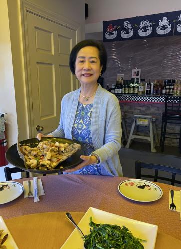 A photo of Alva Mak, owner of Asia Pacific Supermarket & Restaurant in Greenville, SC, holding a Chinese chicken dish.