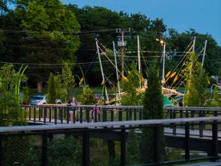 Evening view of Grand Junction Plaza during Jams at the Junction, with a bright moon in the sky above trees, string-lit structures, and people gathered around the railings and walkways.