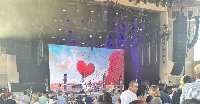 A man in a accessible chair, among concert goers watching a performance on stage..