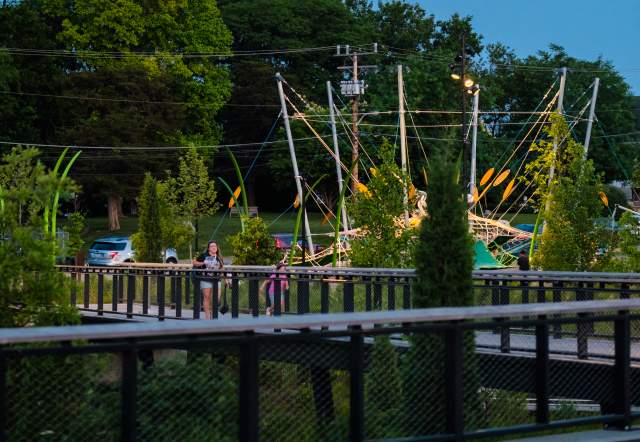 Evening view of Grand Junction Plaza during Jams at the Junction, with a bright moon in the sky above trees, string-lit structures, and people gathered around the railings and walkways.