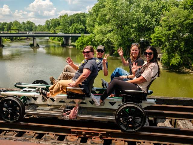 Four people rail biking on a bridge crossing a river