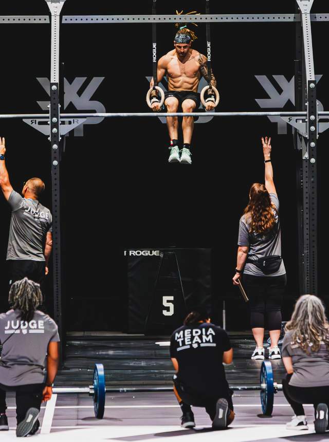 Athletes performing pull-ups during a fitness competition indoors.
