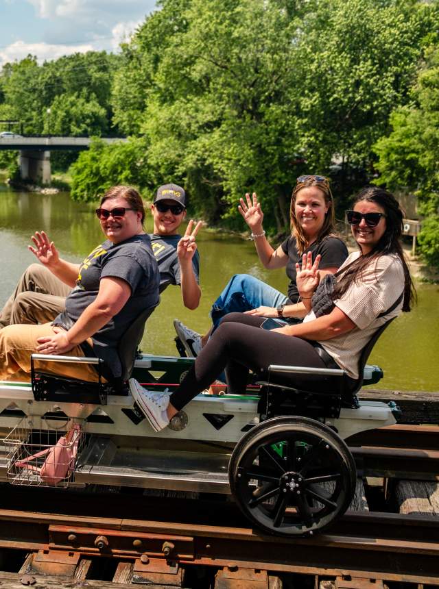 Four people rail biking on a bridge crossing a river