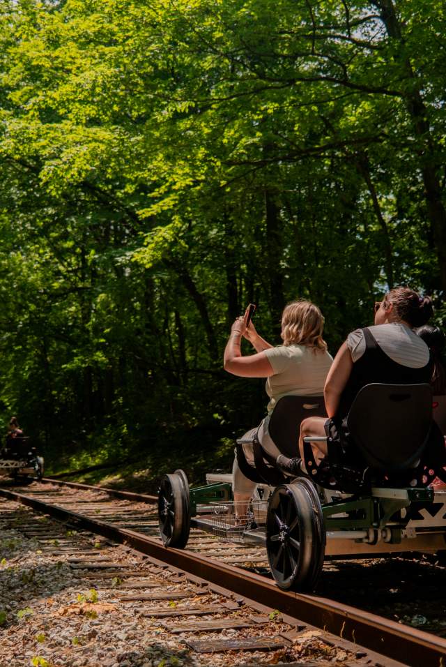 Group riding railbikes along a wooded trail near the Nickel Plate rails.