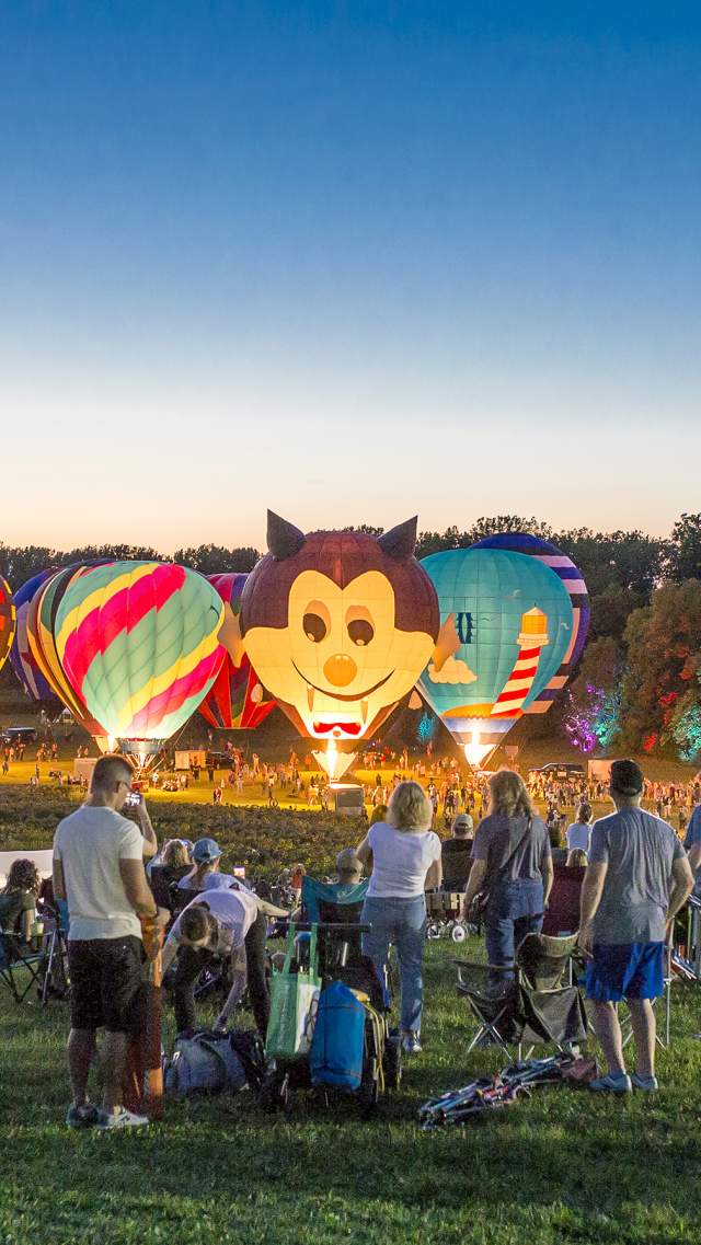 Conner Prairie Jupiter Balloon Flights at night, with several people gathered and large, glowing hot air balloons.