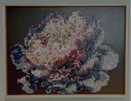 Abstract pixel-style artwork displayed in a light wood frame inside the Fishers Event Center sensory room. The piece features a clustered, cloud-like form made of small colorful squares in shades of pink, purple, blue, and cream against a solid black background.