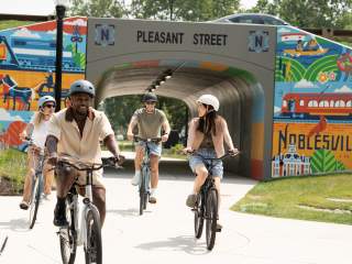 Bikers cycling through the Pleasant Street paved, tunnel-like underpass ,decorated with murals on the Hamilton County Hubway Trails.