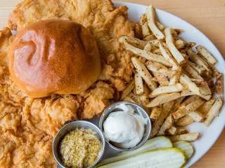 Bread roll over fried chicken, with french fries, butter, mustard and pickles on the side