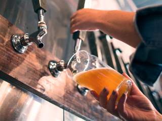 Beer being poured from metal taps into a clear glass at a bar.