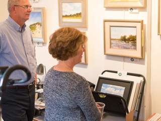 Three people standing inside a gallery or studio space, viewing artwork displayed on a wall.