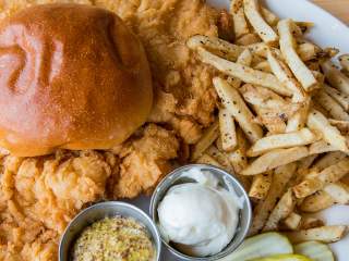 A plate with a tenderloin sandwich, fries, and dips, on a wooden surface.