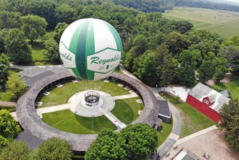 Hot air balloon in vibrant green and white colors floating above a grassy field, trees and a barn below