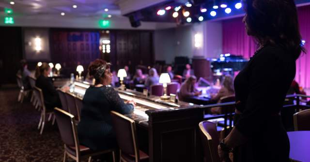 Guests seated at tables and the bar inside Feinstein’s at Hotel Carmichael, lit by stage lights with a performer-ready stage in the background.
