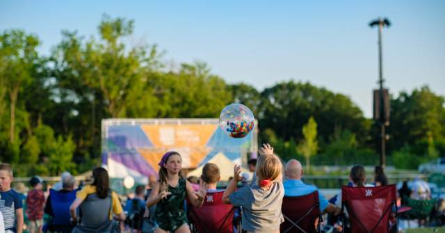 Children play with a clear inflatable ball in front of an outdoor concert audience seated in lawn chairs at Westfield’s Grand Junction Plaza during the Jams at the Junction event.
