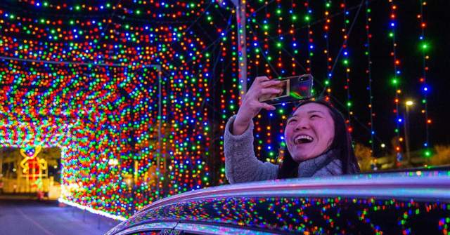 Person taking a cell phone picture in a tunnel covered with holiday lights.