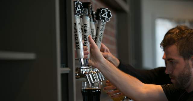 A close-up of a hand pulling a tap handle to pour a drink from a row of numbered metal taps at a bar.