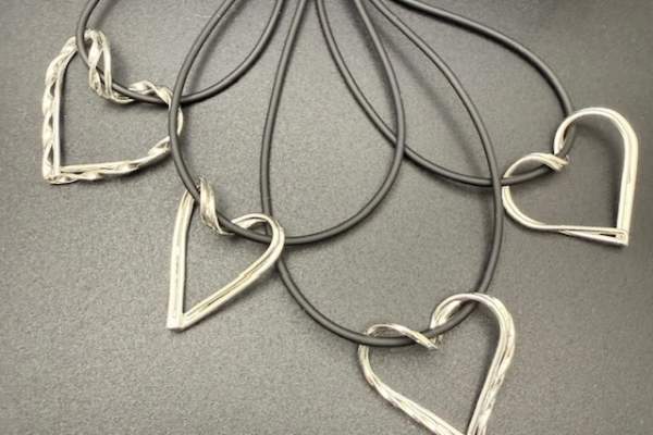 Five metal heart-shaped pendants with a textured, twisted-wire design are attached to black cord loops and arranged in a fan shape on a dark surface.