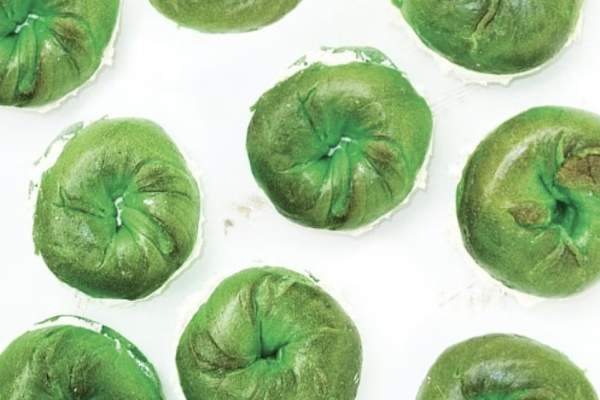 Overhead view of several bright green bagels from Barry Bagels arranged in rows on a white background.