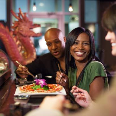 Several people seated at a restaurant table indoors, holding food and smiling in the Arts & Design District.