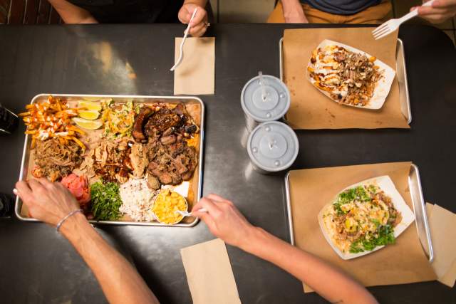 An overhead view of a table with trays of barbecue food and drinks.