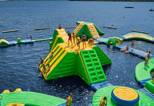 Colorful inflatable water park features climbing structures and slides on a lake, with people enjoying the activities under a clear sky.