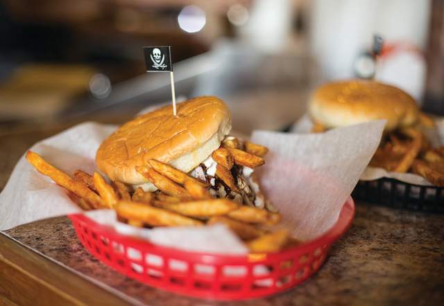 A close-up of a barbecue sandwich topped with fries in a red basket.