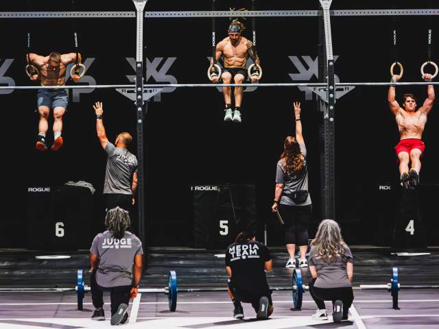 Athletes performing pull-ups during a fitness competition indoors.
