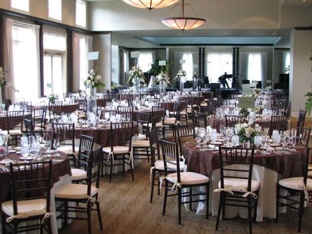 An interior view of a large dining room with numerous round tables set with white cloths and dark chairs.