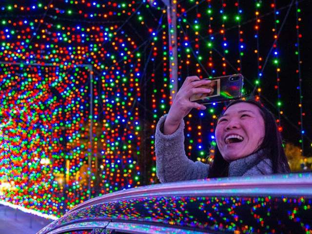 Person taking a cell phone picture in a tunnel covered with holiday lights.