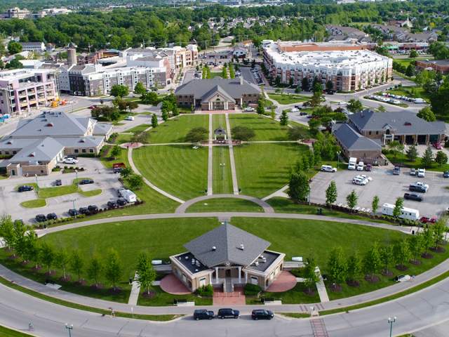 An aerial view of a large, manicured green lawn with symmetrical walking paths, surrounded by modern multi-story brick buildings.