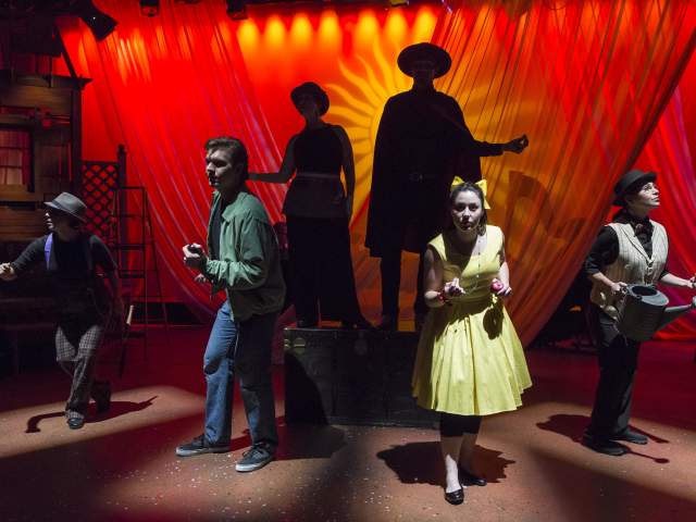 Actors and actresses performing on a stage with a bright red background