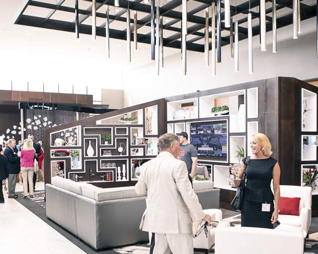 A modern hotel lobby with a sleek gray-and-white interior, featuring open seating areas and clean lines. Several people are gathered throughout the space.