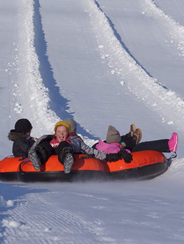 A family sliding down the hill in the snow at Koteewi Run Snow Tubing Park.