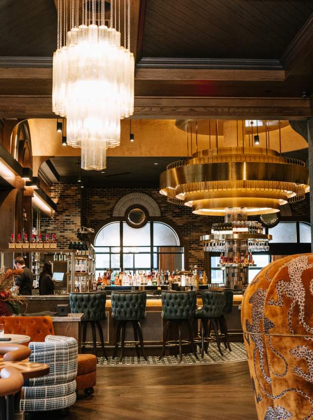 Elegant lounge featuring a gold-accented bar, patterned upholstered seating, and large cascading chandeliers.