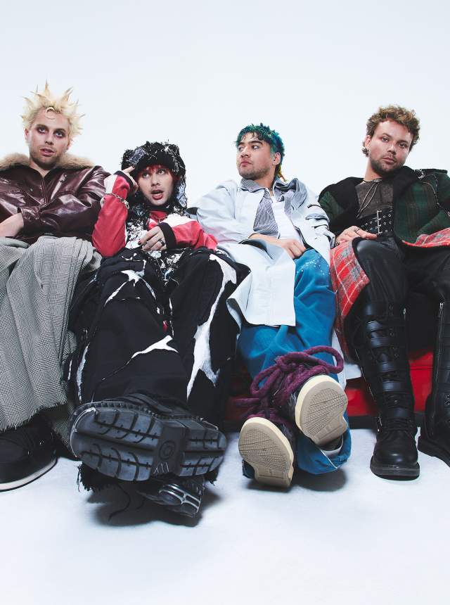 Four people in punk‑inspired outfits sit side by side on a bright red couch against a white background, wearing layered skirts, boots, plaid, and edgy streetwear styles.