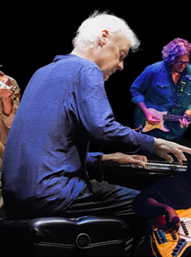 Promotional image of a live music ensemble featuring a pianist at center stage surrounded by musicians playing violin, guitar, bass, keyboards, and drums against a black background.