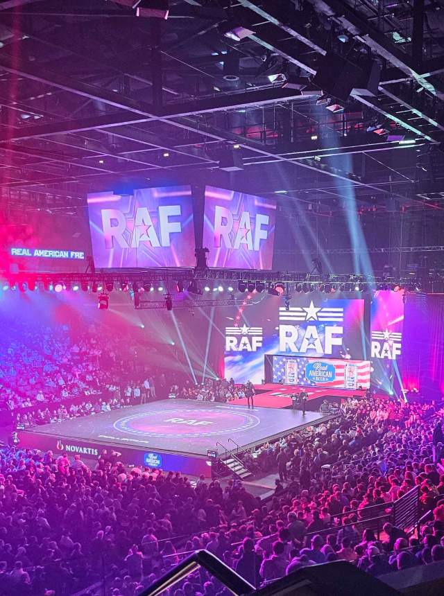 A huge stadium filled with people and a large monitor reading "RAF" with colorful lighting.