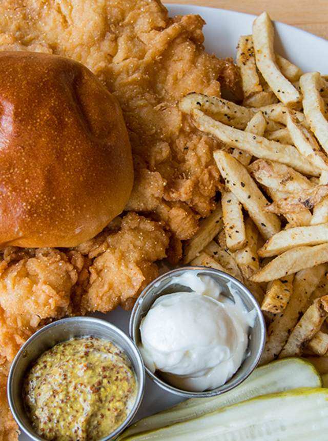 Bread roll over fried chicken, with french fries, butter, mustard and pickles on the side