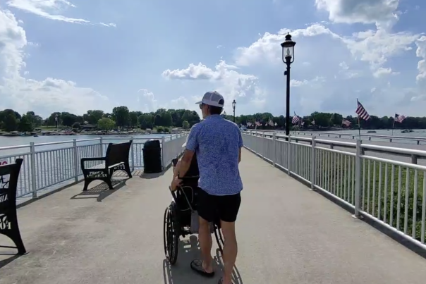 Person using a wheelchair on an accessible bridge with wide pathways, railings, and scenic waterfront views.