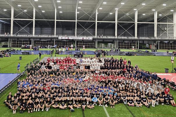 Large group of USA Wrestling athletes and staff on the field at an indoor stadium.