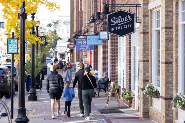 A bustling street scene featuring shop storefronts with colorful signs and a person sitting on a bench.