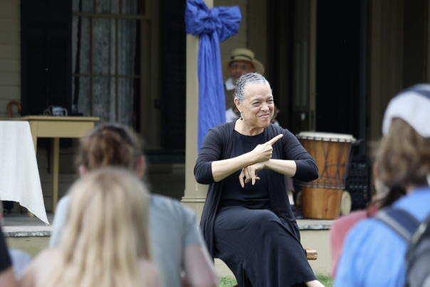 Presenter using hand gestures while speaking to an audience at an outdoor event.