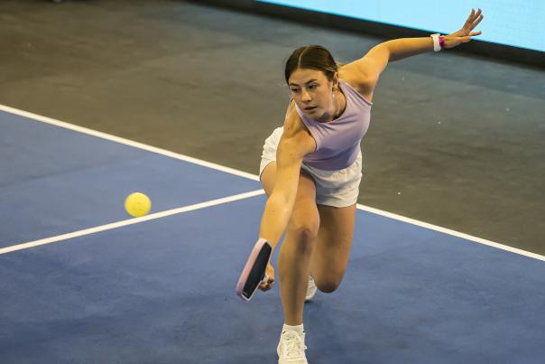 Woman hitting a forehand shot during an indoor pickleball match on a blue court.
