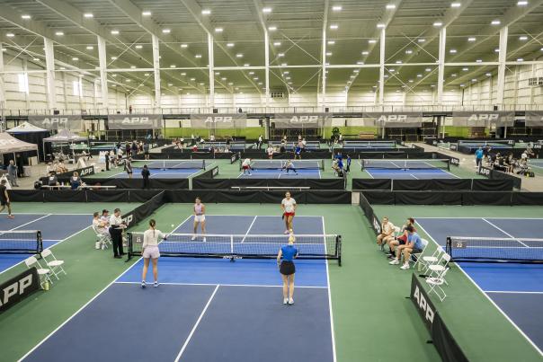 Large indoor pickleball facility with multiple courts and players competing in organized matches.