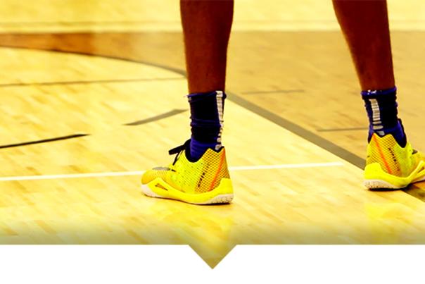 A close-up of a person’s feet wearing bright yellow basketball shoes on a polished indoor wooden court.
